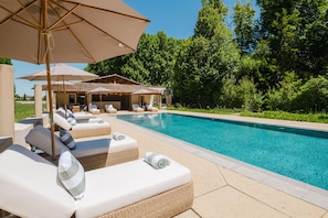 A poolside area with lounge chairs and umbrellas, surrounded by greenery. - Château Saint Perret (Avignon)