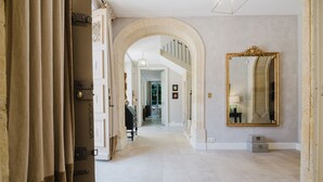 A hallway with a large mirror, a door with a curtain, and a staircase in the background. - Château Saint Perret (Avignon)