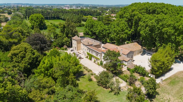 An aerial view of a large estate with multiple buildings, surrounded by dense greenery and a clear sky. - Château Saint Perret (Avignon)