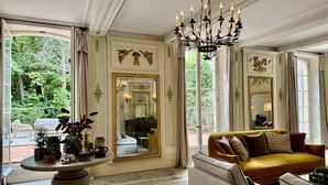 A spacious living room with a large window, a chandelier, and a sofa with cushions. - Château Saint Perret (Avignon)