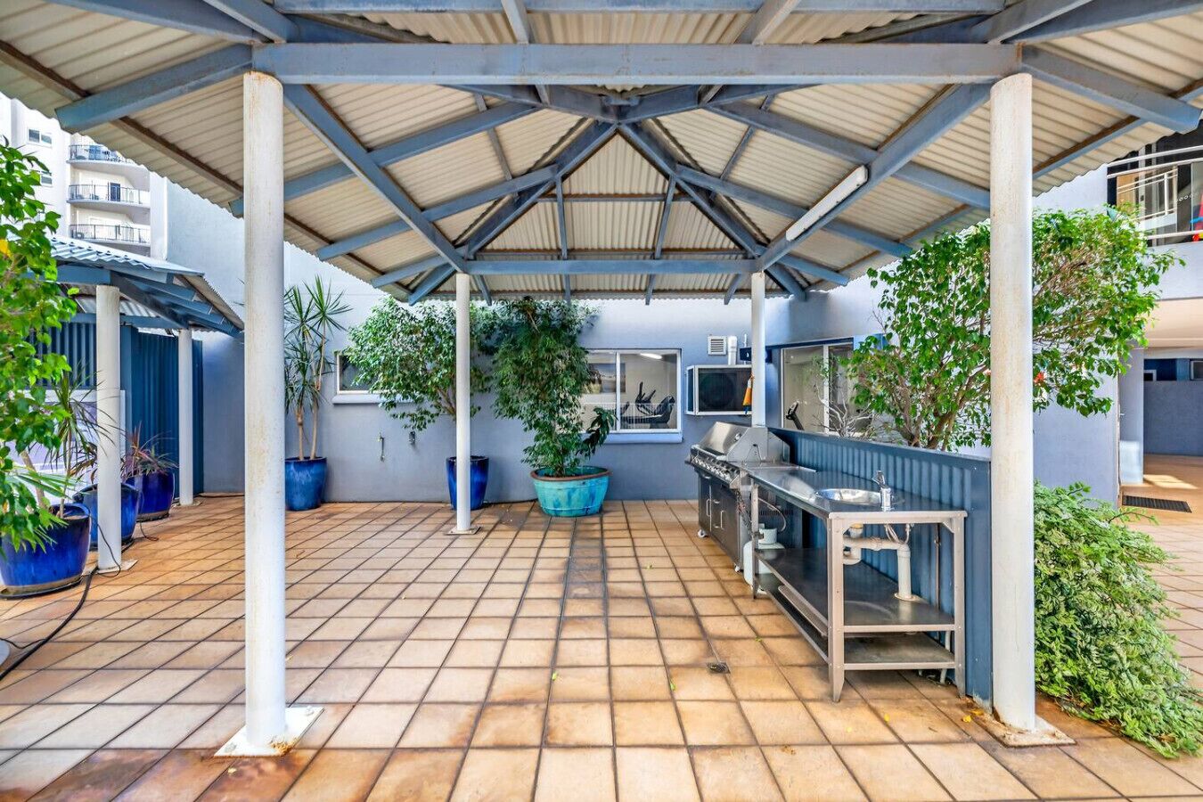 Un'area patio all'aperto con una zona salotto coperta, piante in vaso e un angolo cottura.