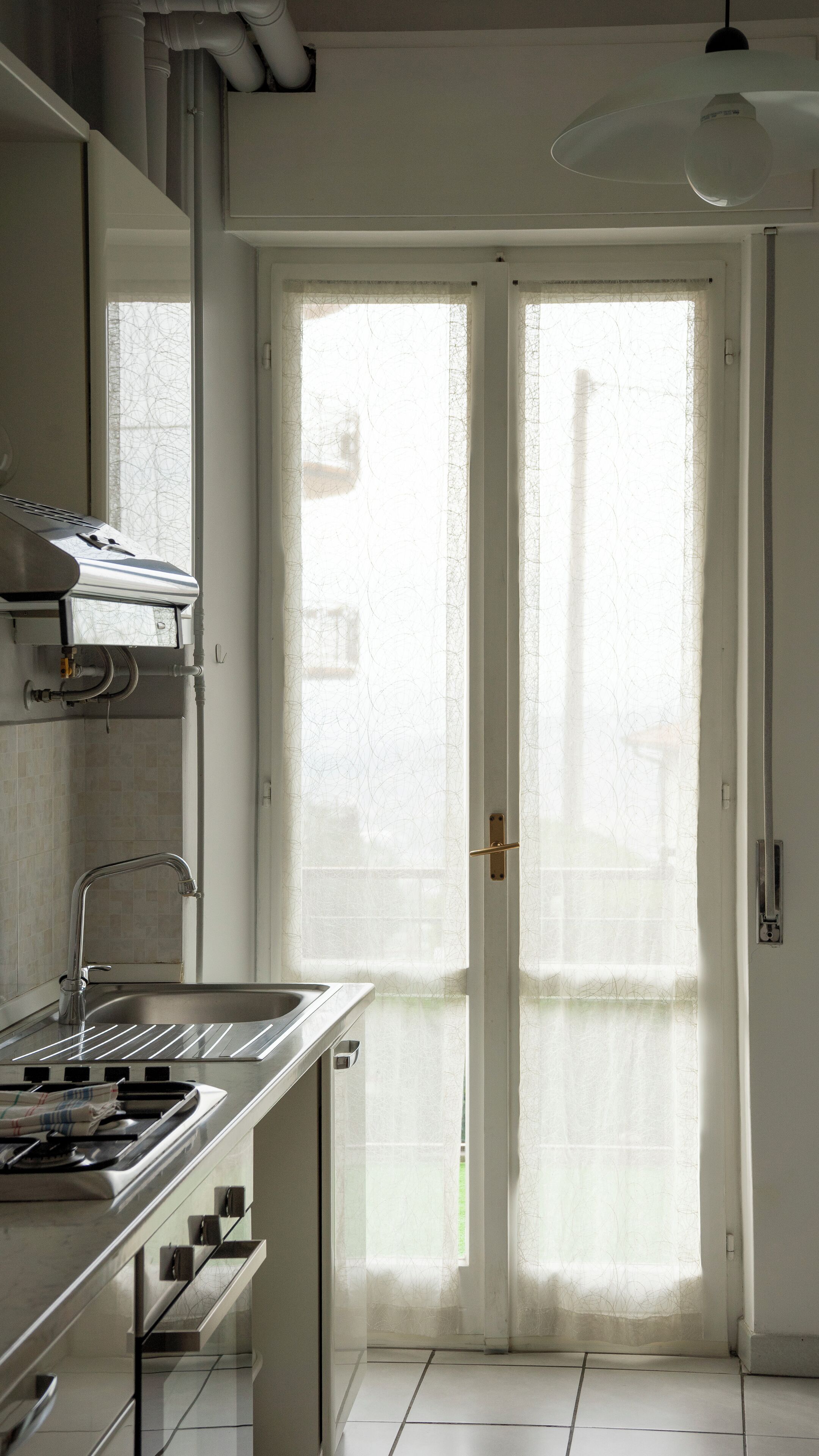 A kitchen with a stove, sink, and a large window with frosted glass doors.