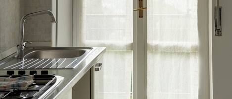 A kitchen with a stove, sink, and a large window with frosted glass doors.
