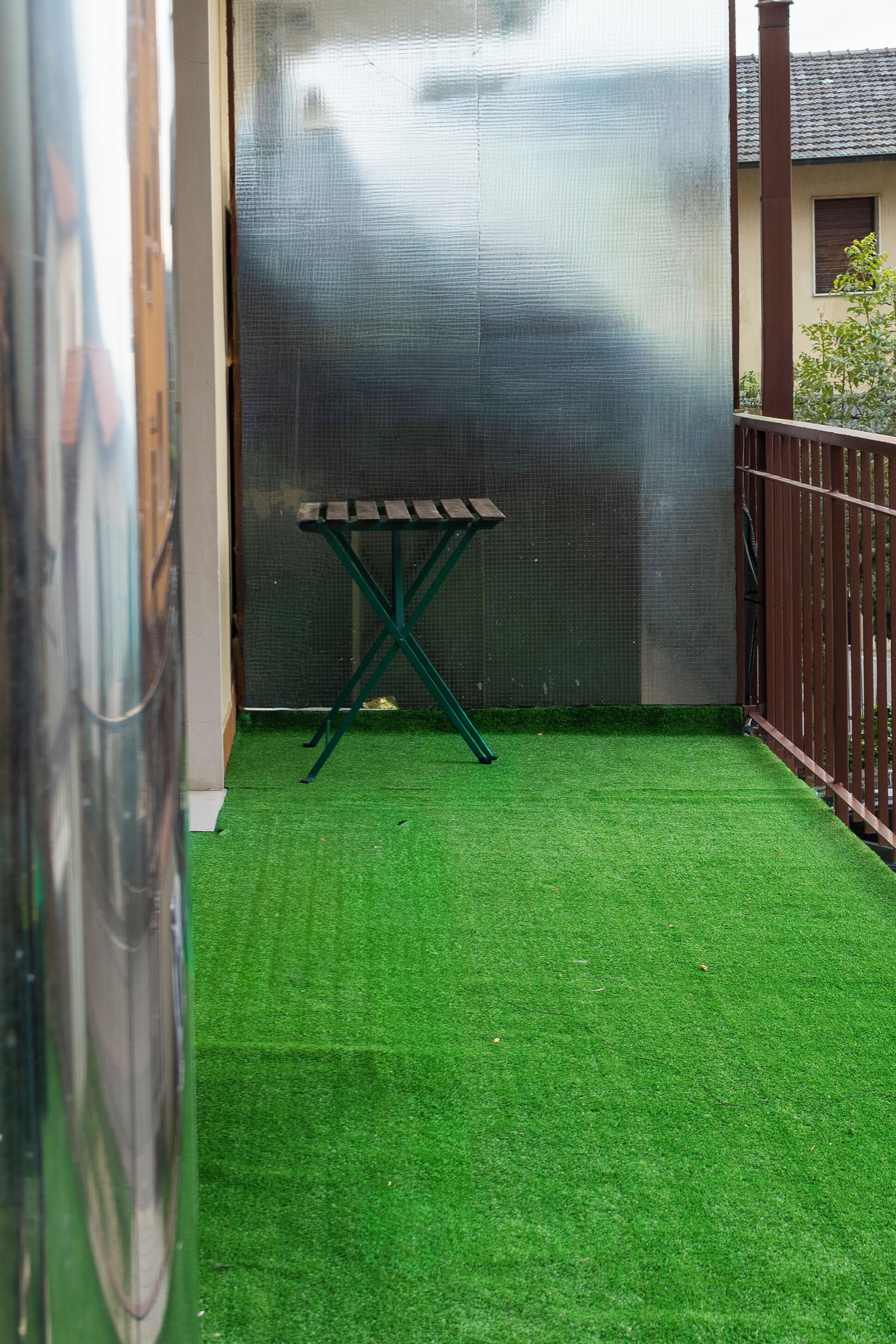 A small enclosed outdoor area with artificial green turf, a metal table, and a metal fence.