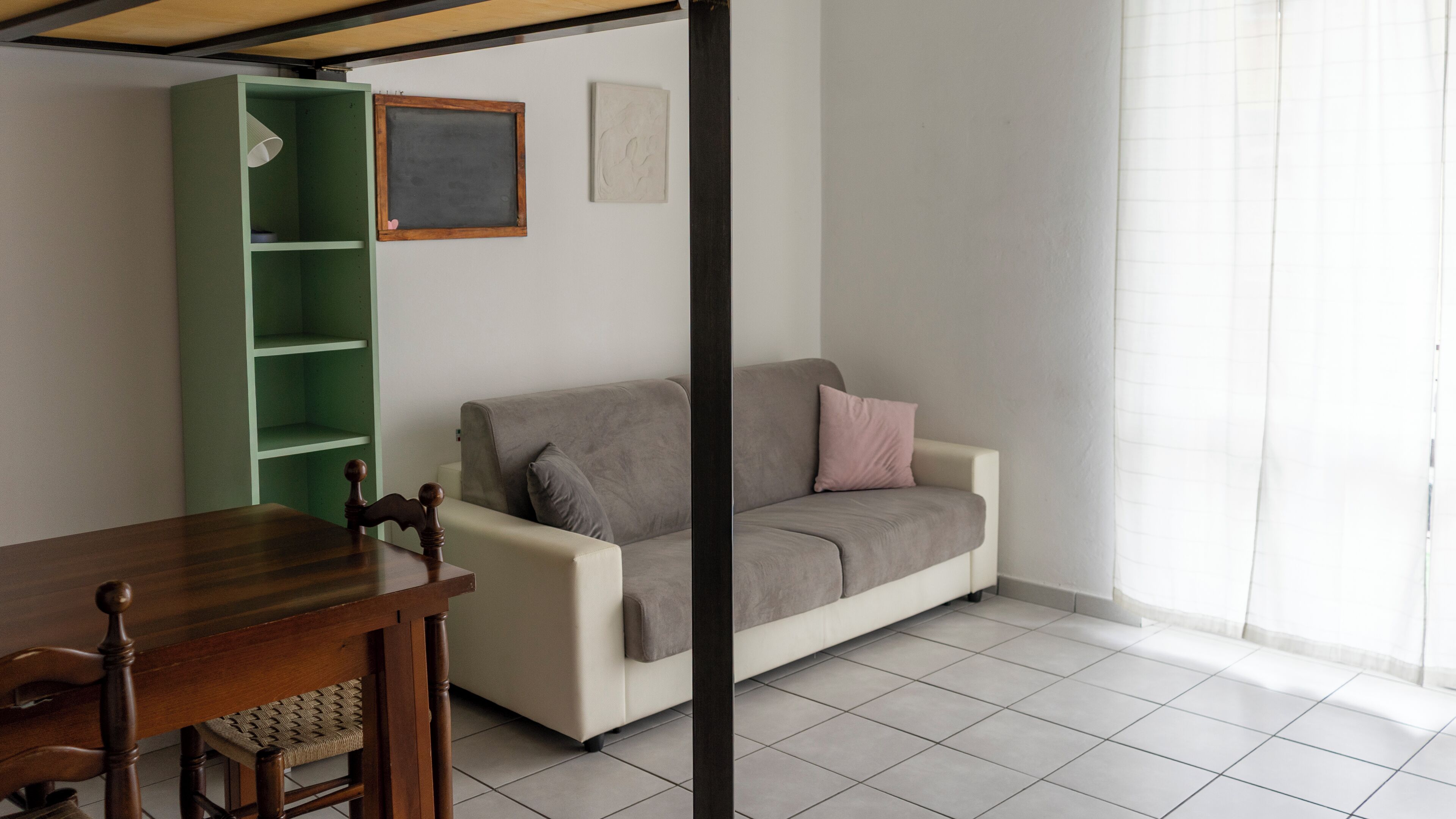 Ein Wohnzimmer mit einer Couch, einem Esstisch und einem grünen Regal.