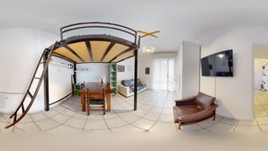 Un vaste espace de vie comprenant une table à manger, un canapé et un téléviseur fixé au mur.