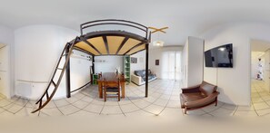Un vaste espace de vie comprenant une table à manger, un canapé et un téléviseur fixé au mur.