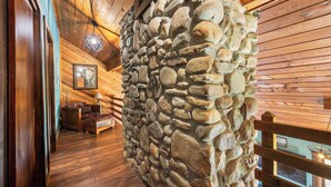 Una habitación rústica con paredes de madera, un muro de piedra, una cama de madera y suelo de madera.