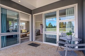 A modern interior with large sliding glass doors leading to a balcony, a seating area with a table and chairs, and a view of a green landscape.