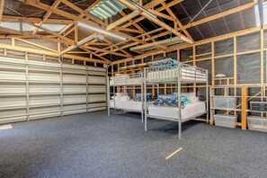 A multi-level bunk bed room with a garage door, metal shelving, and a ceiling with wooden beams.
