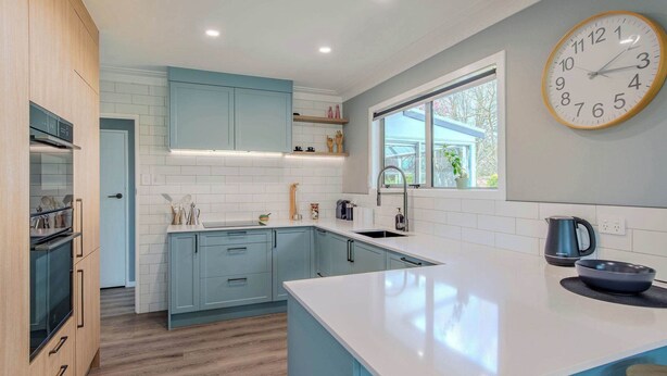 Una cocina moderna con armarios azul claro, encimera blanca y un reloj de pared grande.
