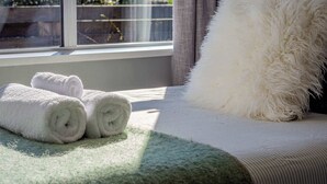 Una cama impecablemente hecha, con toallas blancas enrolladas y un almohadón mullido, ubicada junto a una ventana con vistas a la vegetación.