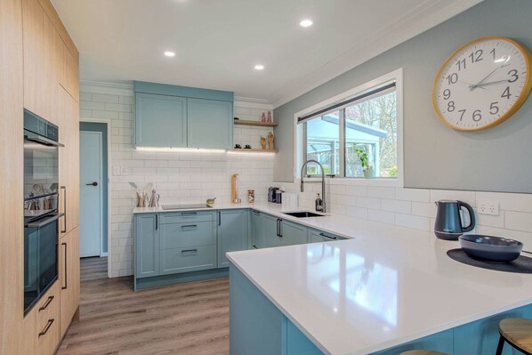 A modern kitchen with light blue cabinets, a white countertop, and a large wall clock.