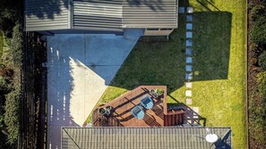 An aerial view of a backyard with a wooden deck, a barbecue area, and a paved patio.