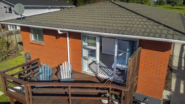 A house with a brick exterior, a tiled roof, and a wooden deck with chairs.