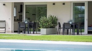 A modern outdoor dining area with a pool, a potted plant, and a sliding glass door leading to a kitchen. - Armonia Suites - Acqua- new apartment with garden and pool in Verona (Verona)
