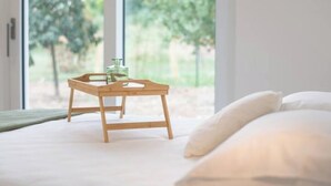 A bedroom with a bed, pillows, a wooden tray with a glass and a bottle, and a view of trees through large windows. - Armonia Suites -Earth and Water new apartments with garden and pool in Verona (Verona)