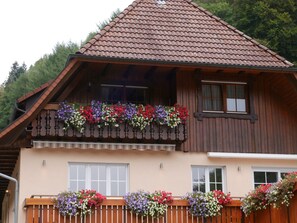 A wooden chalet with a sloped roof, a balcony with flower boxes, and a window with curtains. - Apartment 'Eulennest' with Shared Pool, Private Terrace and Wi-Fi (Wolfach)