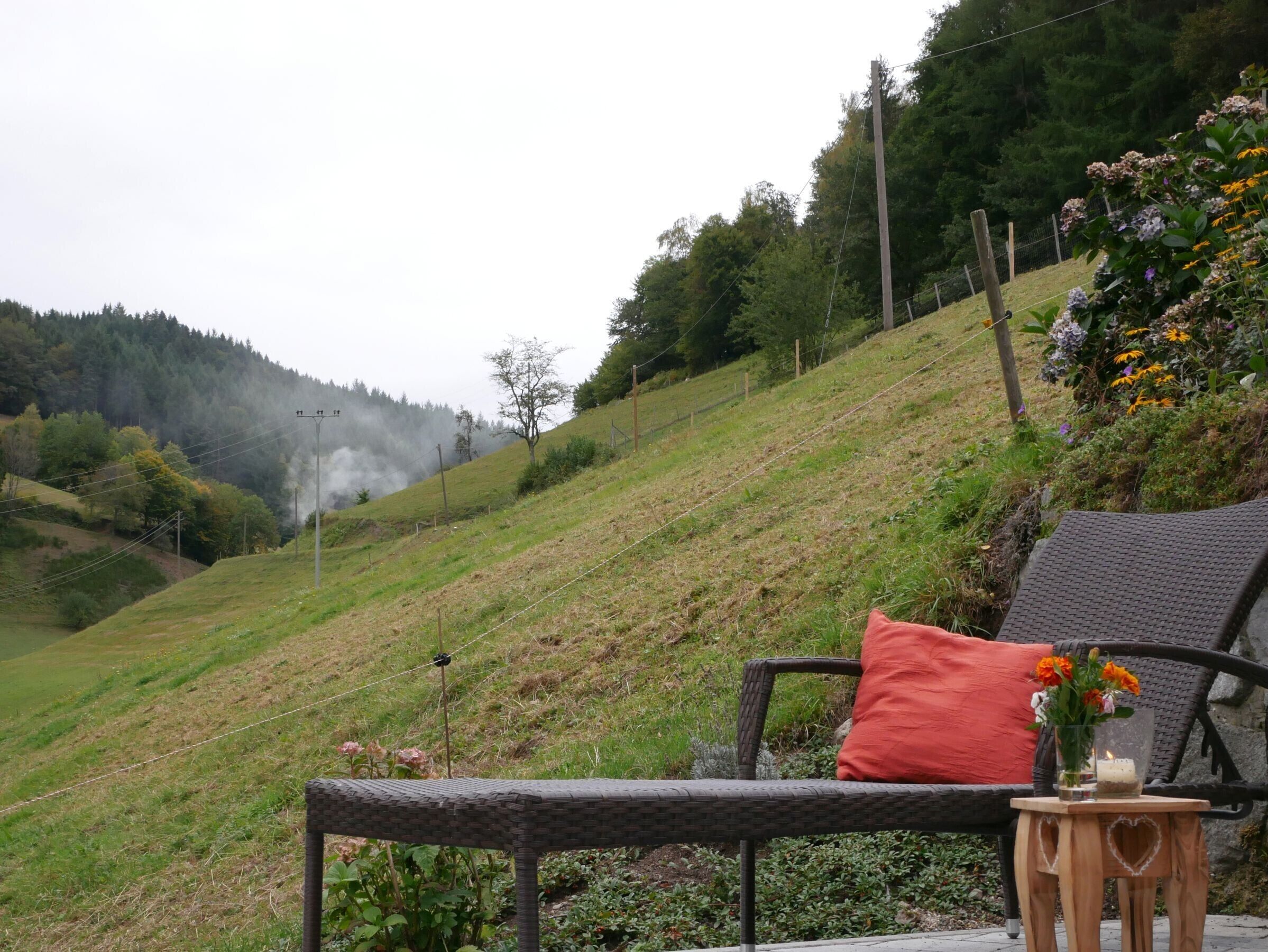 Ein Korbstuhl mit rotem Kissen und einem kleinen Holztisch mit Kerze und Blumen.