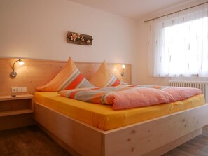 A bedroom with a wooden bed, two bedside lamps, a nightstand, and a window with sheer curtains. - Apartment 'Eulennest' with Shared Pool, Private Terrace and Wi-Fi (Wolfach)