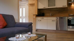 Eine moderne Küche mit Edelstahlgeräten, einem Glastisch mit Kerzen und einem grauen Sofa mit rotem Kissen.