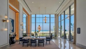 A spacious room with a large window offering a view of the beach, a dining area with a table and chairs, and a modern chandelier. - Deluxe 1-BR Sea view Address Beach Marassi (El Alamein)