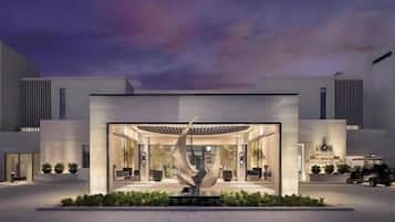 A modern building with a central atrium, large windows, and a landscaped area with a sculpture.