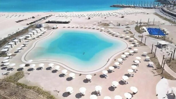 An aerial view of a beach resort with a large central pool, sun loungers, and a pier extending into the sea. - Deluxe 1-BR Sea view Address Beach Marassi (El Alamein)
