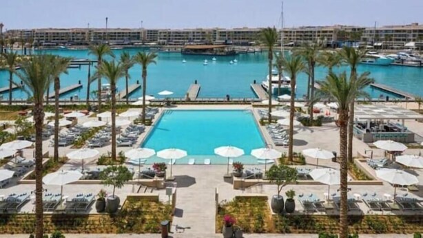 A resort pool area with a view of the marina, lounge chairs, and palm trees.