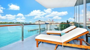 Ein Balkon mit zwei Liegestühlen mit Blick auf ein Gewässer, einen klaren Himmel und ein weit entferntes Kreuzfahrtschiff.