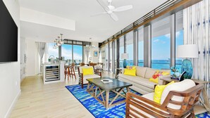 Ein modernes Wohnzimmer mit großem Fenster, Deckenventilator und Essbereich mit Stühlen und Tisch.
