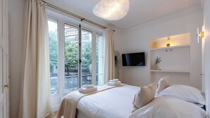 A bedroom with a large bed, a TV mounted on the wall, and a window with curtains. - Charming Flat - 2bd/6p - Passy / Eiffel Tower (Paris)