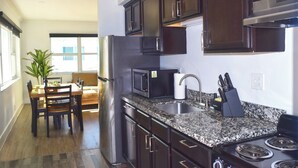 Una cocina moderna con gabinetes de madera oscura, electrodomésticos de acero inoxidable y encimeras de granito, junto con un comedor con mesa y sillas.