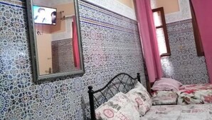 Ein Schlafzimmer mit einer Wand aus gemusterten Fliesen, einem Bett mit floralem Bettzeug und einem an der Wand montierten Fernseher.