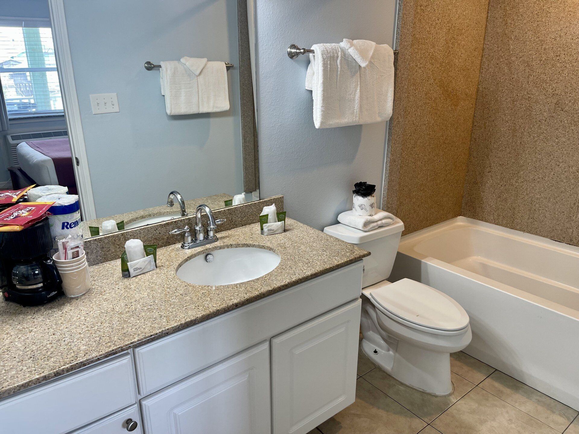 A bathroom with a granite countertop sink, a mirror, a toilet, and a bathtub.