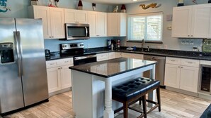 A modern kitchen with white cabinets, a stainless steel refrigerator, a microwave, and a central island with a bench. - Beachgate Condo Suites And Hotel 211+212+213 3 Bedroom Condo (Port Aransas)
