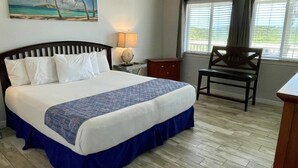 A neatly arranged bedroom with a bed, a chair, a nightstand, a lamp, and a window with curtains. - Beachgate Condo Suites And Hotel 211+212+213 3 Bedroom Condo (Port Aransas)