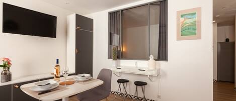 A modern kitchen with a flat-screen TV, a dining table with chairs, a bar area, and a window with curtains.