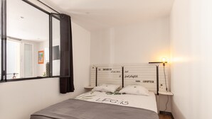 Quarto com cama, mesa de cabeceira, espelho e luminária na parede.
