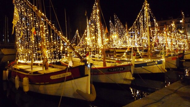 Uma marina à noite com barcos atracados, iluminada por luzes de Natal.