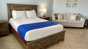 A bedroom with a wooden bed, a beige sofa, and a nightstand with a lamp.