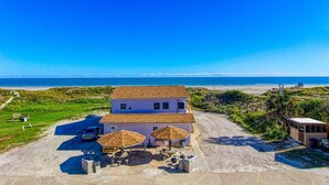 A two-story house with a beach view, a parking area, and outdoor seating with umbrellas. - Beachgate Condo Suites And Hotel 234+235+236 3 Bedroom Condo (Port Aransas)