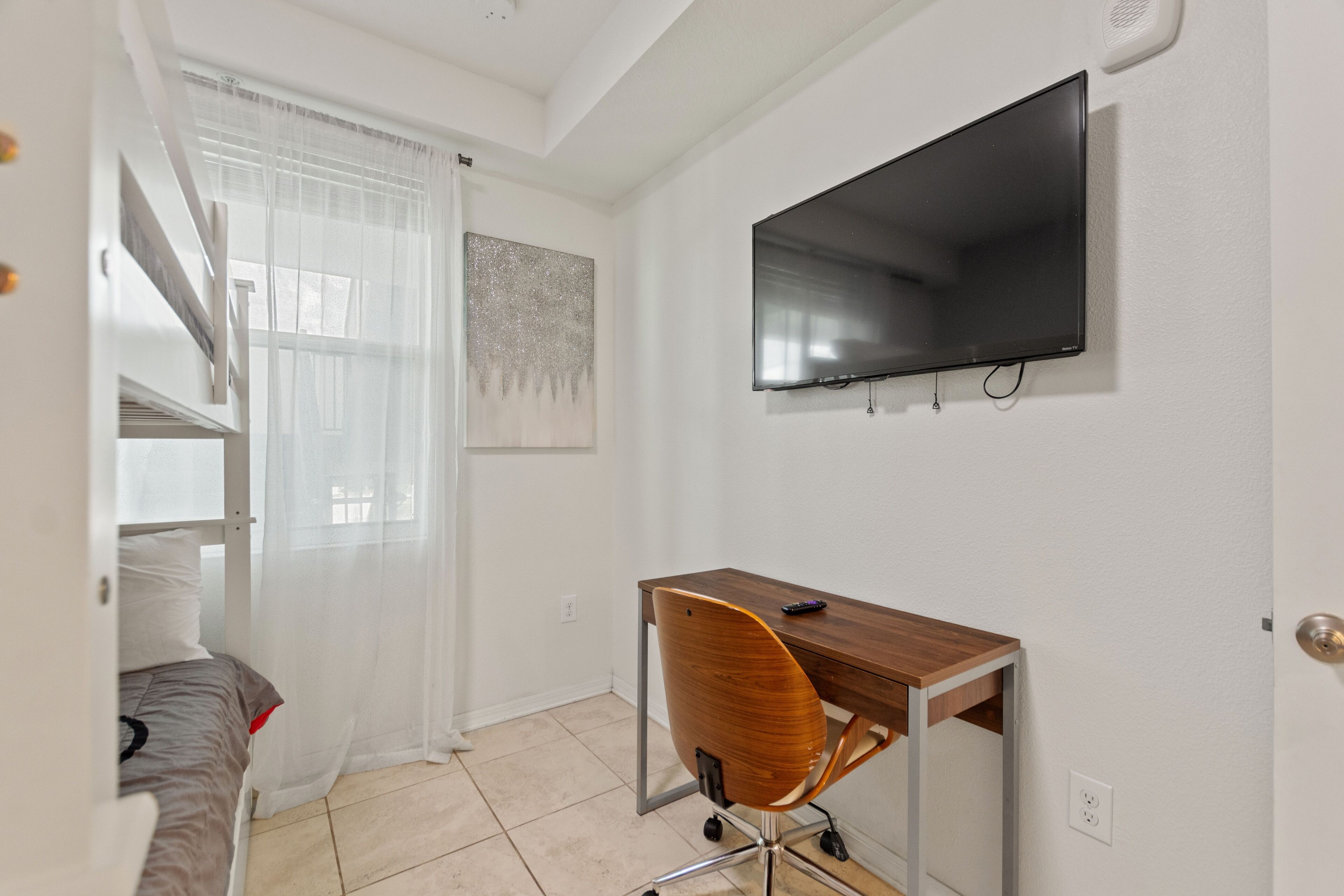 A bedroom with a bed, a desk, and a TV mounted on the wall.