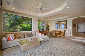 A spacious living room with a large window, a ceiling fan, and a dining area with a wooden table and chairs. - Makena Surf, #b-208 2 Bedroom Condo (Kihei)