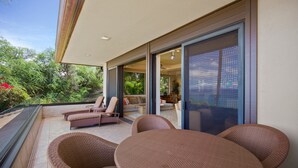 A covered outdoor seating area with wicker furniture, a glass door leading to an interior space, and a view of greenery. - Makena Surf, #b-208 2 Bedroom Condo (Kihei)