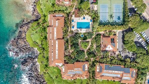 An aerial view of a coastal property with a swimming pool, tennis courts, and a rocky shoreline. - Makena Surf, #b-208 2 Bedroom Condo (Kihei)