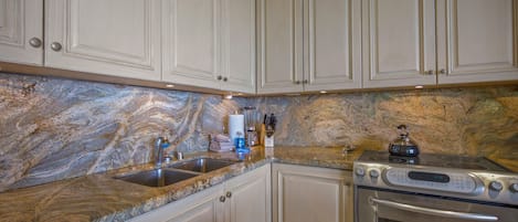 A kitchen with white cabinetry, a granite countertop, a stainless steel stove, and a built-in oven.