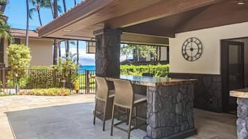 Un patio al aire libre con un bar de piedra, dos sillas de mimbre y un reloj en la pared.