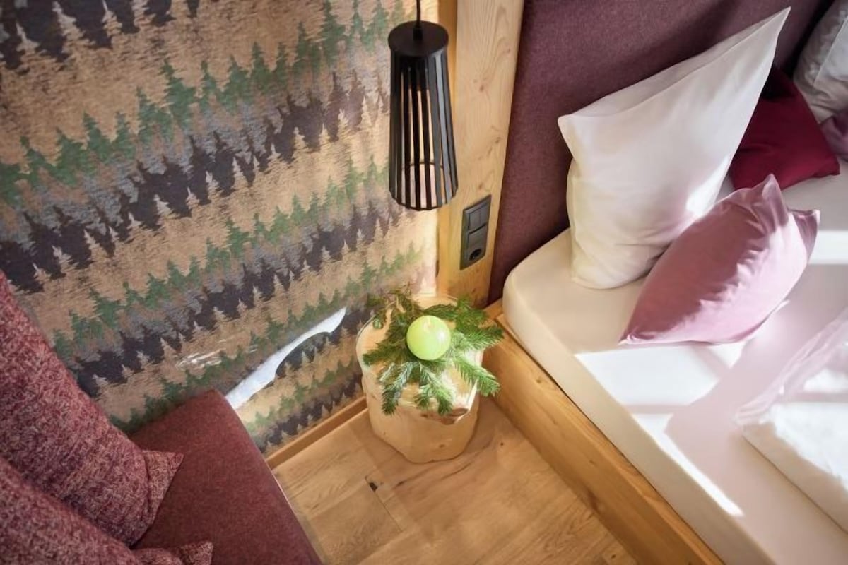 A cozy room with a bed, a hanging light fixture, and a wall with a forest pattern.
