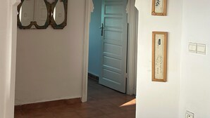 Un pasillo con suelo de baldosas, una puerta blanca y dos cuadros enmarcados en la pared.